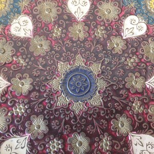 May include: A close-up of a decorative round tray with a red background and intricate gold and white floral designs. The centre of the tray features a blue and gold starburst pattern.