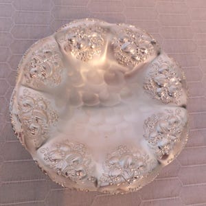 May include: A silver-plated bowl with a scalloped edge and embossed floral design. The bowl has a hammered finish and is perfect for serving fruit or snacks.