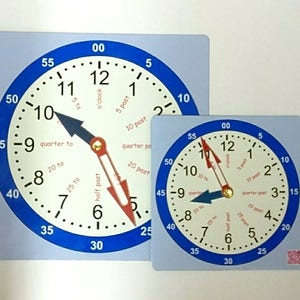 May include: Two blue and white educational clocks. The larger clock shows the time as ten to six, with a blue hour hand and a red minute hand. The smaller clock shows the time as ten to three. Both clocks have a blue border.