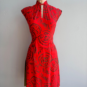 May include: A red dress with a mandarin collar and a keyhole neckline. The dress has a dark brown geometric pattern. The dress is displayed on a vintage dress form.