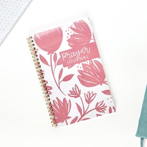 May include: A pink and white prayer journal with a floral design. The cover says "prayer journal" in white script.