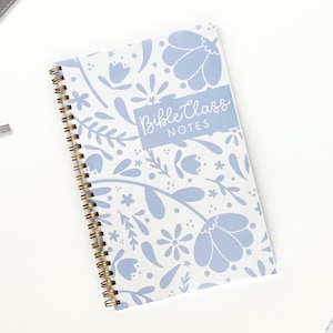 May include: A spiral-bound notebook with a floral pattern in light blue and white. The cover features the text "Bible Class NOTES" in a light blue rectangle. The notebook has a gold-colored spiral binding.