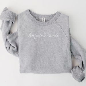 Peut inclure: Un sweat-shirt gris chin&eacute; avec le texte "love God + love people" en lettres blanches en cursive.