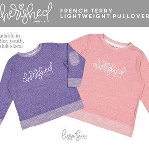 May include: Two long-sleeved sweatshirts with a heather purple and a heather pink color. Both sweatshirts have a white graphic that says "cherished 1 John 3:1" with a small heart above the word "cherished".