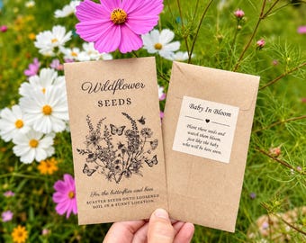 May include: Two seed packets, one labeled "Wildflower Seeds" with a floral and butterfly illustration, and the other "Baby In Bloom." The packets are brown, held against a backdrop of colorful flowers.