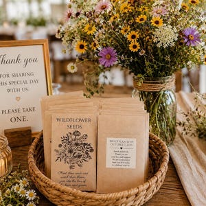 May include: A woven basket filled with rectangular brown paper seed packets featuring black floral illustrations and text that reads Wildflower Seeds, Bruce & Kaitlyn October 7 2025, and a sign that reads Thank you for sharing this special day with us.