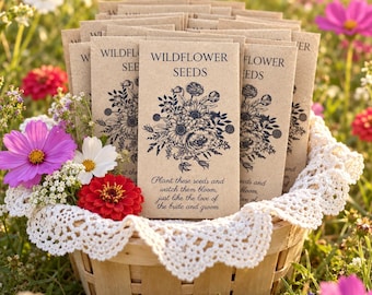 May include: A collection of rectangular kraft paper seed packets labeled Wildflower Seeds with a black floral illustration and the text Plant these seeds and watch them bloom, just like the love of the bride and groom, arranged in a wooden basket.