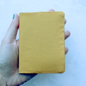 May include: A small, mustard yellow fabric pouch with a folded edge. The pouch is held in a hand.
