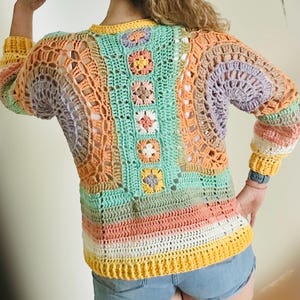K&ouml;nnte beinhalten: Ein bunter H&auml;kelpullover mit geometrischem Muster in Gr&uuml;n-, Orange-, Gelb- und Lilat&ouml;nen. Der Pullover hat eine lockere Passform und lange &Auml;rmel.