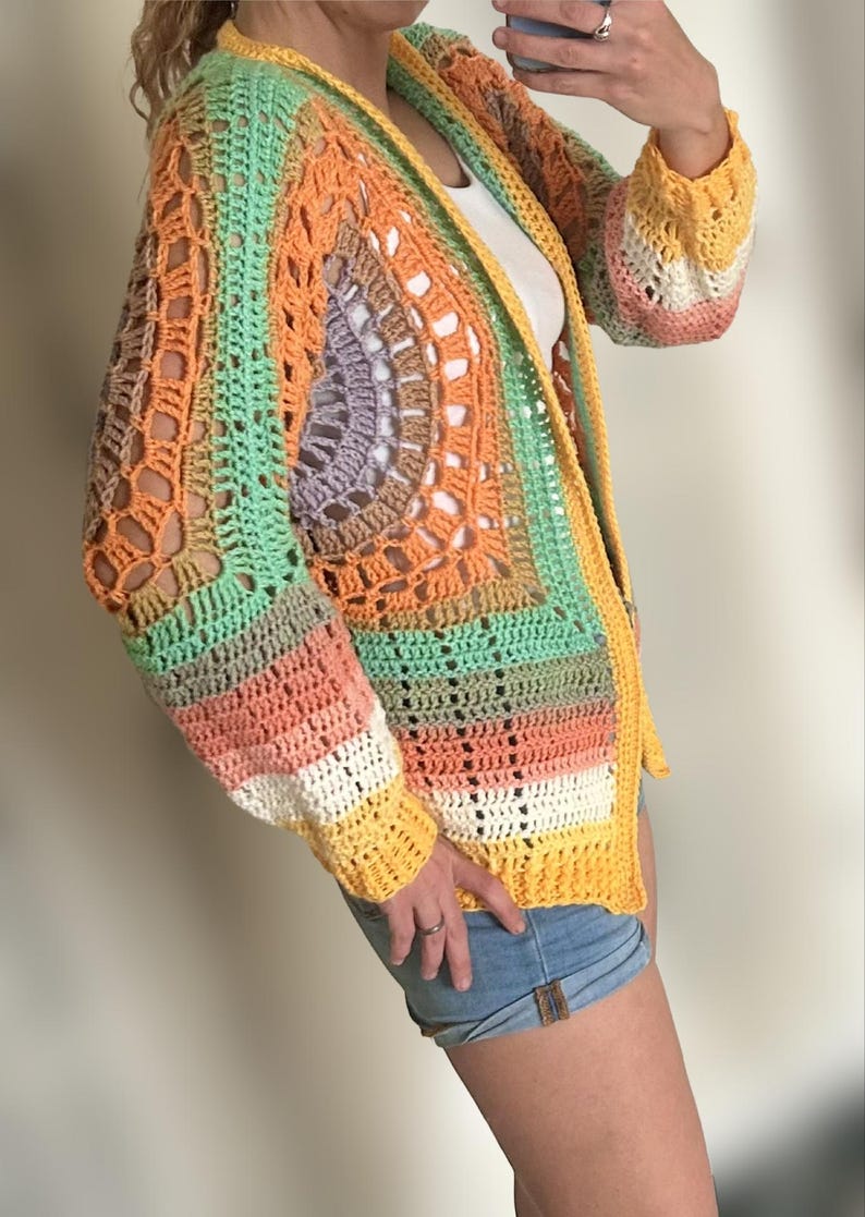 K&ouml;nnte beinhalten: Ein farbenfroher H&auml;kelcardigan mit einem Regenbogenstreifenmuster. Der Cardigan hat eine lockere Passform und eine lange L&auml;nge. Er ist aus verschiedenen Farben gefertigt, darunter Orange, Gelb, Gr&uuml;n und Pink.