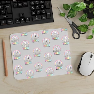 Puede incluir: Una alfombrilla de ratón gris con un patrón repetido de un esqueleto con un arcoíris detrás y el texto "Everything Sucks" en un círculo blanco.