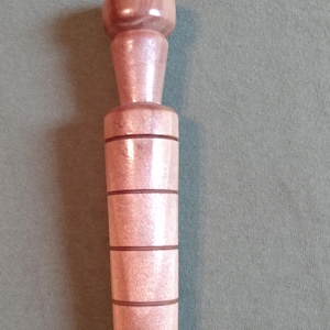 May include: A light brown wooden bottle stopper with a rounded top and a cylindrical body. The body has four dark brown bands. The stopper is designed to fit into a bottle.