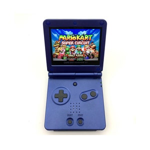 Puede incluir: Una consola de juegos portátil Game Boy Advance SP azul con una pantalla brillante que muestra el juego "Mario Kart Super Circuit". La consola tiene un pad direccional negro, dos botones negros y un botón de inicio y selección.