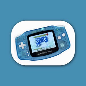 May include: A translucent blue Game Boy Advance handheld gaming console featuring a lit screen displaying the Super Mario Advance 4: Super Mario Bros. 3 title screen. The device includes a directional pad, A and B buttons, and Start and Select buttons.