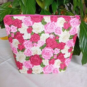 May include: A pink zippered pouch with a floral print of white and pink roses.