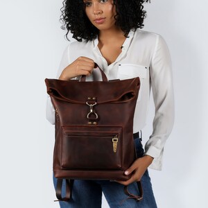 Handmade leather backpack, dark brown, with a unique roll-top design and front zipper pocket for easy access. This durable and stylish backpack features a spacious interior, suitable for outdoor adventures and daily commutes.