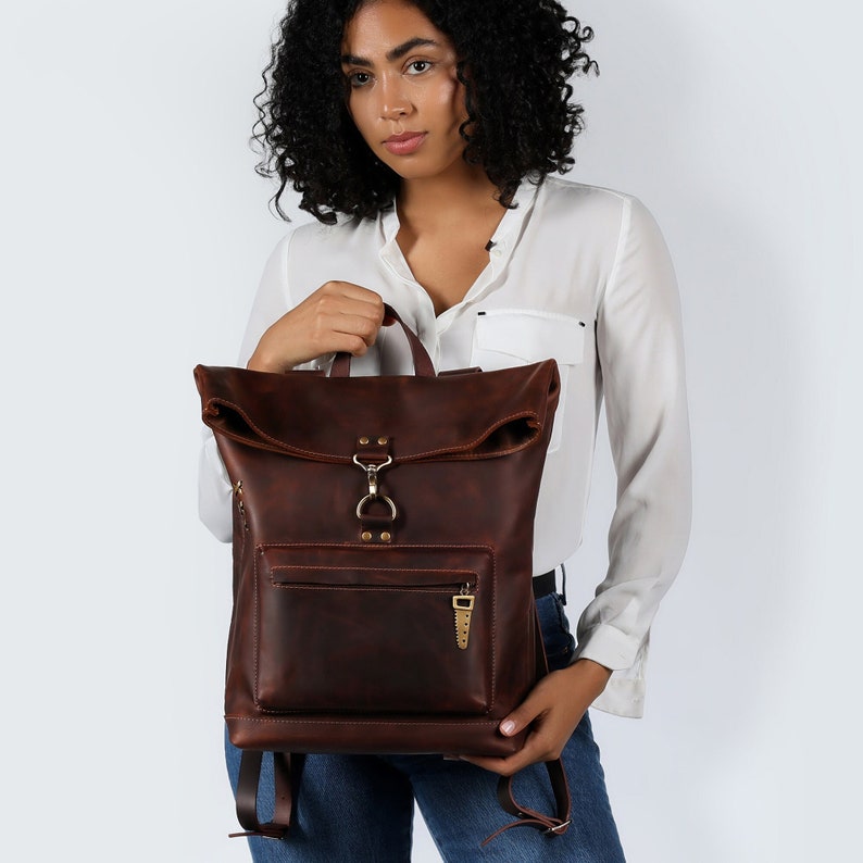 Handmade leather backpack, dark brown, with a unique roll-top design and front zipper pocket for easy access. This durable and stylish backpack features a spacious interior, suitable for outdoor adventures and daily commutes.