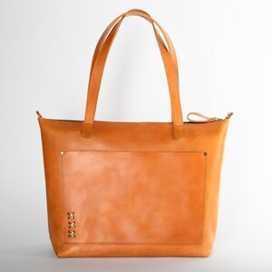 A durable full-grain leather tote bag with a matte honey finish, designed to last.a large light cognac purse with a spacious front pocket, made from genuine thick honey-colored leather.