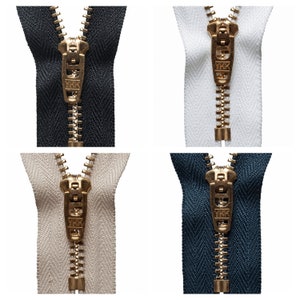 May include: Four different zipper pulls with gold metal sliders and teeth. The zippers are in four different colors: black, white, beige, and navy blue.