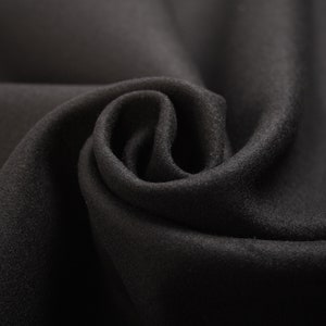 Puede incluir: Primer plano de una tela negra con una superficie suave y texturizada. La tela está doblada y drapeada, creando una curva suave y fluida.