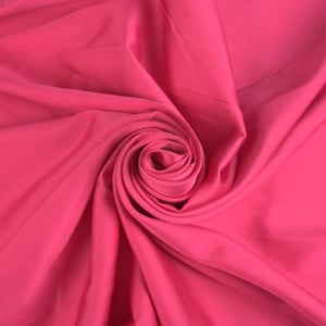 Könnte beinhalten: Nahaufnahme eines leuchtend pinkfarbenen Stoffes, der zu einer Rosenform gefaltet und gedreht ist.