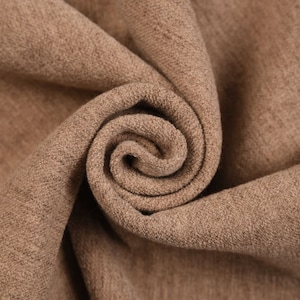 Könnte beinhalten: Nahaufnahme eines braunen Stoffes mit strukturierter Oberfläche. Der Stoff ist gefaltet und zu einer Spirale gedreht.