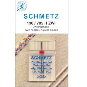 May include: A close-up of a package of Schmetz twin needles, labeled "130/705 H ZWI". The package is white with blue and red accents. The needles are visible inside the package.