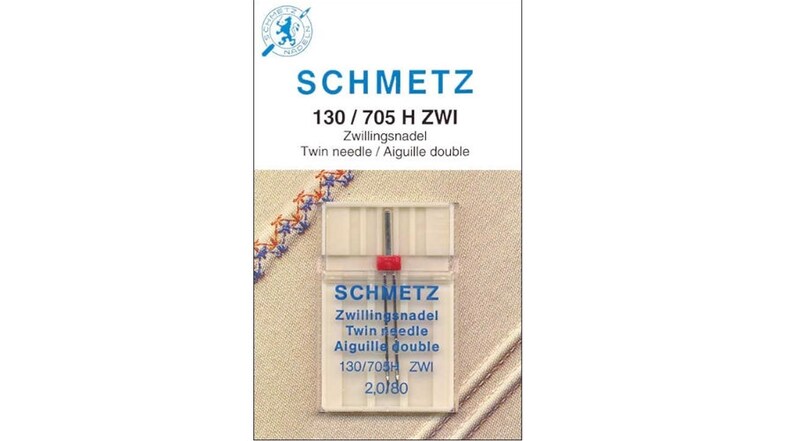 May include: A close-up of a package of Schmetz twin needles, labeled "130/705 H ZWI". The package is white with blue and red accents. The needles are visible inside the package.