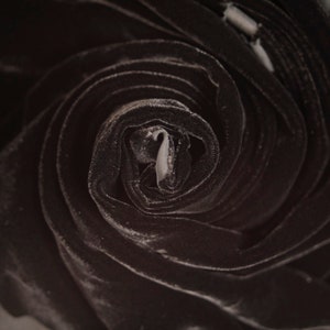 May include: Close-up of a black velvet fabric rolled into a spiral shape. The fabric is soft and luxurious, with a subtle sheen.