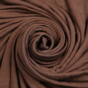 Könnte beinhalten: Nahaufnahme eines braunen Stoffes, der zu einer Spirale gedreht ist. Der Stoff ist weich und glatt und hat einen dezenten Glanz.