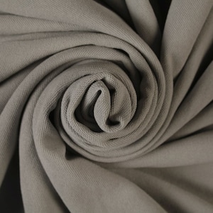 May include: A close-up of a gray fabric with a textured surface. The fabric is folded and twisted into a spiral shape.