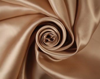 Puede incluir: Primer plano de una tela suave, lisa y lujosa de color marrón claro. La tela está drapeada y doblada para crear un patrón en espiral con forma de rosa.