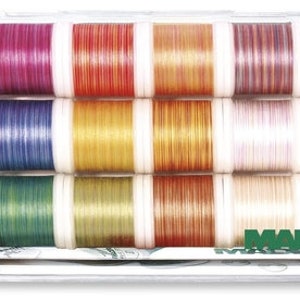 May include: A clear plastic box containing 16 spools of Madeira embroidery thread. The spools are arranged in four rows of four. The thread colours are a mix of light and dark shades, including pink, blue, green, yellow, and brown.