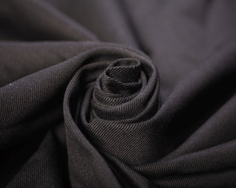 Könnte beinhalten: Nahaufnahme eines schwarzen Stoffes, der zu einer Rosenform gefaltet ist. Der Stoff hat eine subtile Textur und ein weiches, fließendes Gefühl.
