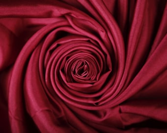 May include: A close-up of a deep red fabric swirled into a rose shape.