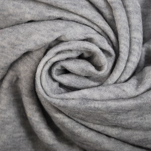 Op de afbeelding: Close-up van een grijze stof, opgerold in een spiraalvorm. De stof heeft een zachte textuur met subtiele kleurschakeringen. De plooien en schaduwen creëren een interessant patroon. Geschikt voor textielprojecten.