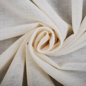 Pode incluir: Um close-up de um tecido de algodão branco, dobrado e torcido em forma de espiral. O tecido é macio e texturizado, com um brilho sutil.