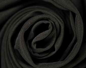 Könnte beinhalten: Nahaufnahme von schwarzem Stoff, der zu einer Rosenform gefaltet ist. Der Stoff hat eine glatte, leicht strukturierte Oberfläche.