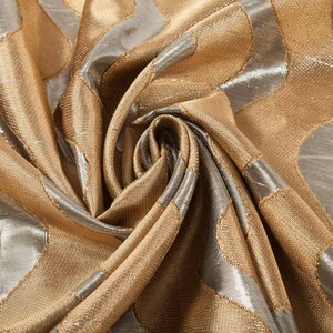 May include: Close-up of a gold and silver fabric with a textured, geometric pattern. The fabric is folded and draped, showing the intricate details of the design.