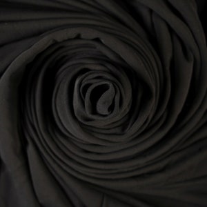 Peut inclure: Tissu noir enroulé en spirale, créant un fond sombre et texturé.
