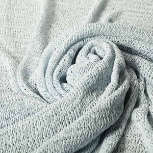Può includere: Un tessuto di maglia blu chiaro con una trama a trama aperta. Il tessuto è piegato e attorcigliato a forma di spirale.