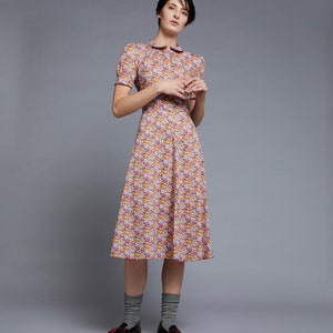 May include: A woman wearing a yellow and blue floral print dress with a white collar and short sleeves. She is wearing dark brown loafers and grey socks.