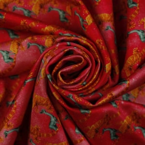 Op de afbeelding: Rode satijnen stof met een herhalend patroon van gouden en groene gestileerde giraffen.