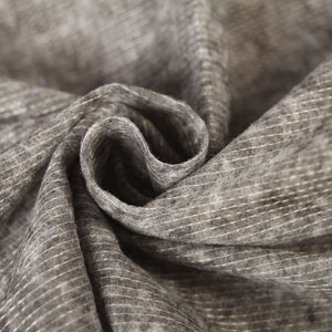 May include: Close-up of a gray fabric with a subtle striped pattern. The fabric is folded and twisted, creating a textured and abstract design.