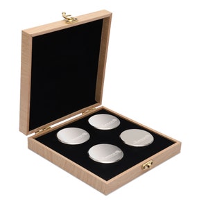 Puede incluir: Una caja de madera con interior negro y cierre dorado. La caja contiene cuatro objetos redondos de color plateado con la palabra "Switchcraft" grabada en cada uno.