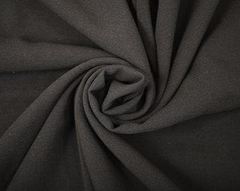 May include: Close-up of a black fabric with a textured surface. The fabric is folded and twisted, creating a swirling pattern.