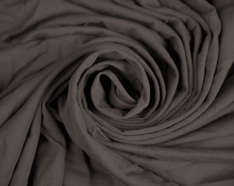 May include: Close-up of a dark brown fabric with a soft, smooth texture. The fabric is folded and twisted into a spiral shape, creating a visually appealing pattern.