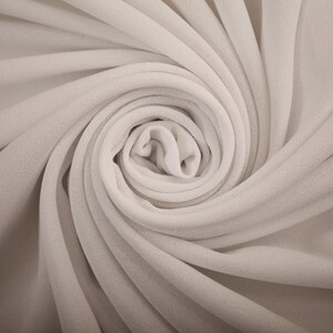 Könnte beinhalten: Nahaufnahme eines weißen Stoffes, der zu einer Spirale gedreht ist. Der Stoff ist weich und glatt und erzeugt eine zarte und elegante Textur.