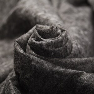 Puede incluir: Primer plano de una tela gris doblada en forma de rosa. La tela es suave y texturizada, creando un diseño delicado y elegante.