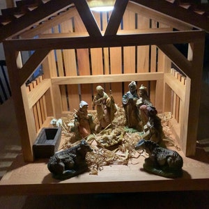 May include: A wooden nativity scene with figurines of Mary, Joseph, baby Jesus, and the three wise men. The scene is lit by a small light bulb in the roof of the structure.